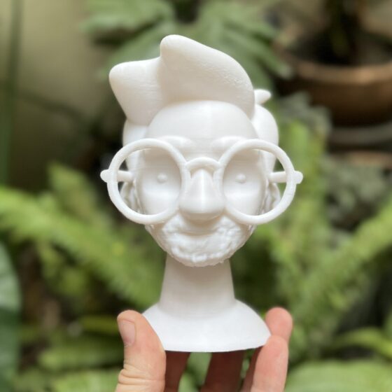 Foto de un busto, impreso en 3D, de la cabeza de un hombre con lentes. El rostro tiene facciones simplificadas, estilo caricatura.